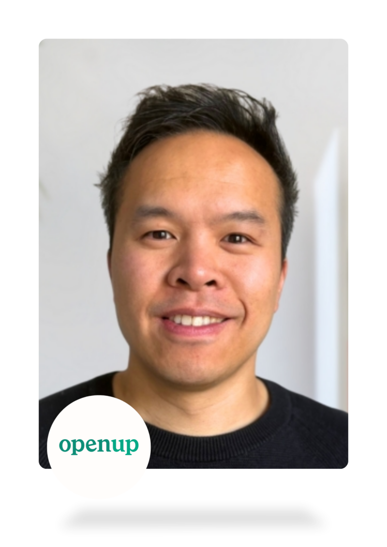 Eine lächelnde Person mit kurzen dunklen Haaren und einem schwarzen Hemd, die in einer gut beleuchteten Umgebung in die Kamera schaut. Das openup-Logo erscheint in der unteren linken Ecke des Bildes.
