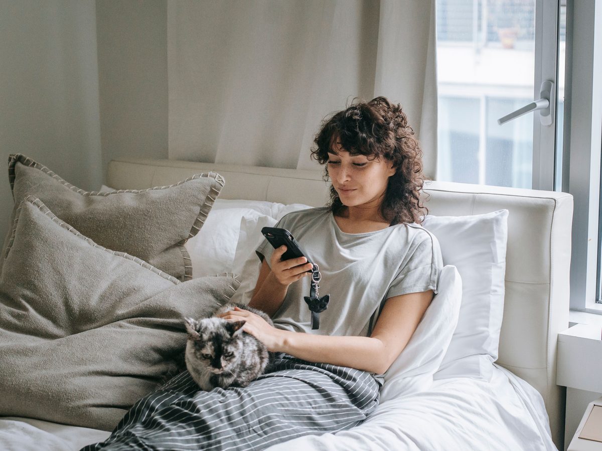 An employee at home in the morning, her cat beside her, messaging the AI Welzijnscoach on her phone