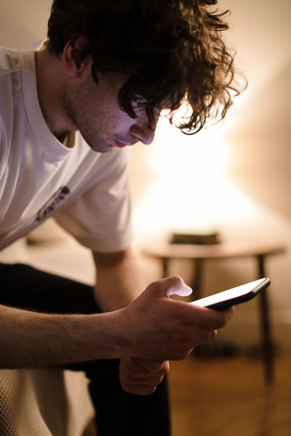 A person sitting with a phone in a softly lit room at night.