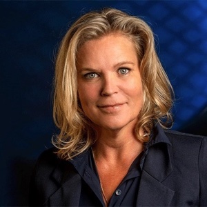 Annet Scheeren, Head of Sustainable Employability bij Rabobank, met blond schouderlang haar en een donkerblauw jasje, voor een donkerblauwe achtergrond.