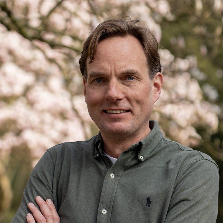 Gijs Coppens, psycholoog, CEO en oprichter van OpenUp, met zijn armen over elkaar voor een bloeiende magnolia.